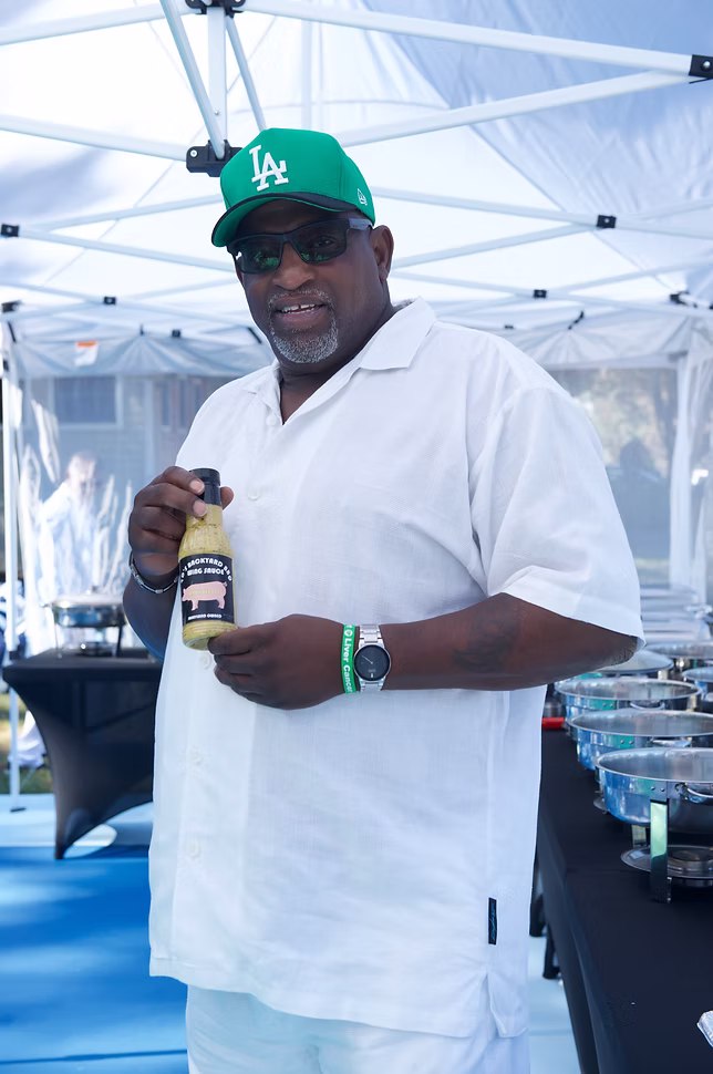 TD holding a bottle of his sauce at an outdoor table